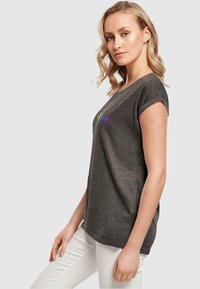 Graues Kurzarm-T-Shirt mit Rundhalsausschnitt und dem Wort "Hoffnung" in Regenbogenfarben auf der Vorderseite gestickt. Weiche Textur.