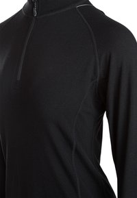 Sort langærmet top med høj krave og kvart lynlås. Har et tætsiddende design, glat tekstur og kontrasterende syninger langs sømmene.