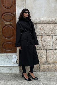 Čierny trenčkot s opaskom, veľkými gombíkmi a širokými rukávmi. Nosí sa s čiernymi stiletto topánkami a legínami. Pozadie z kamennej a drevenej steny.