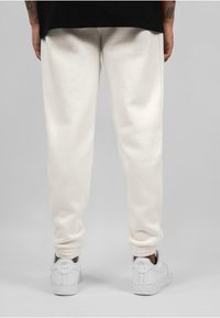 Hvite bomulls-joggebukser med elastiske mansjetter, som har en glatt tekstur. Kombinert med hvite sneakers. Bakgrunnen er nøytral grå.