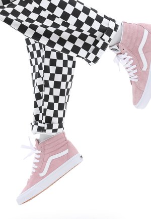 Rosa semskede høyhælte sneakers med hvite detaljer, kombinert med svart-hvitt rutete bukser som viser et geometrisk mønster og cropped design.