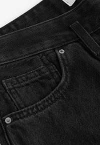 Zwarte denim jeans met een close-up van de tailleband en zak. De stof toont een gestructureerde weving, met zichtbare stiksels en een metalen knoop.