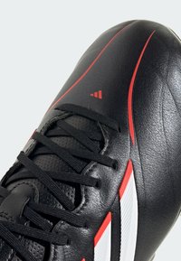 Schwarzer Sportschuh aus Leder mit roten und weißen Akzenten, schwarzen Schnürsenkeln und einem kleinen roten, dreieckigen Logo im Zehenbereich.