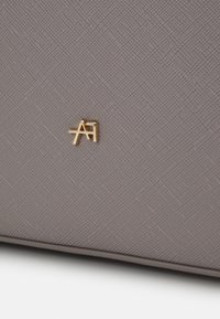 Bolsa de material texturizado gris con un detalle en oro del logo "A". La superficie presenta un patrón sutil y un diseño estructurado.