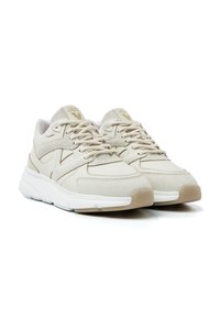 Beige sportieve schoenen met mesh en leren panelen, textuur details, ronde neus, gevoerde zool en vetersluiting. Gouden logo accent zichtbaar.