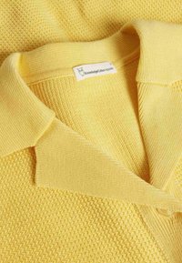 Gelbes gestricktes Poloshirt mit strukturierter Musterung, flachem Kragen und Knopfdetails, mit einem Etikett von KnowledgeCotton Apparel.
