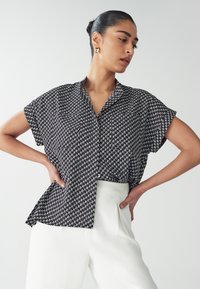 Zwart-wit gestreepte blouse met korte mouwen en kraag, losse pasvorm, knoopdetails, gecombineerd met witte hoge taillebroeken.