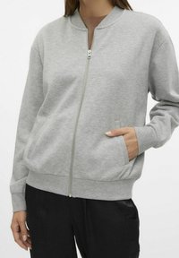 Szara bluza na zamek wykonana z miękkiego materiału, z wysokim kołnierzem, ściągaczami na rękawach i bocznymi kieszeniami. Gładka faktura i luźny krój.