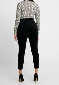Femme de dos, portant un haut à motif serpent à manches longues, un pantalon noir taille haute et des chaussures à talons noirs.