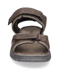 Ruskeat nahkasaappaat, joissa säädettävät remmit, tekstuuri harmaa pohja ja pehmustettu sisäpohja. Avoin muotoilu hengittävyyden takaamiseksi.