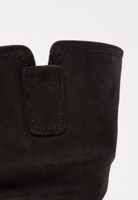 Guante de cuero negro con una textura suave, con un puño corto y un acento cosido en la parte superior. Abierto en la muñeca para facilitar su uso.