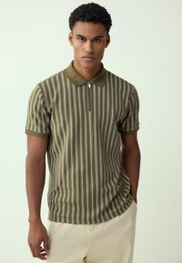 Groen gestreepte polo shirt met een ritskraag, met smalle witte strepen en een gestructureerd patroon. Draagt met lichte broek.