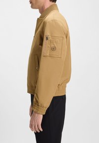 Khaki tuulelõhkuja jope soonikkoega krae ja mansettidega. Omadused hõlmavad tõmblukuga käselagune taskut, küljetaskuid ja elastset äärt. Sile, kerge kangas.