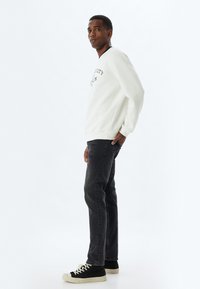 Sudadera blanca con texto negro, jeans grises y zapatillas negras con suela blanca. La sudadera tiene un cuello redondo y puños acanalados.