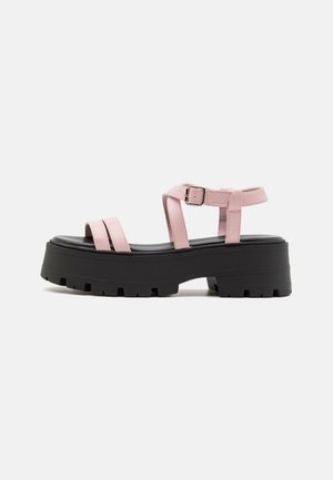 Sandali platform rosa con suola nera spessa, caratterizzati da due ampie cinghie frontali e una fibbia alla caviglia. Texture liscia e design moderno.