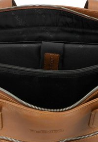Borsa per laptop in pelle marrone con chiusura a zip e un interno in tessuto nero dotato di più scomparti e un'etichetta con logo cucita.