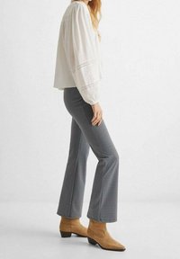 Vit, texturerad blus med elastiska manschetter som kombineras med mönstrade, figurnära svartvita utsvängda byxor och beige ankelstövlar.