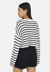 Czarny i biały paskowany sweter o kroju cropped z długimi rękawami, wykonany z dzianiny, w zestawie z czarnymi szortami o wysokim stanie.