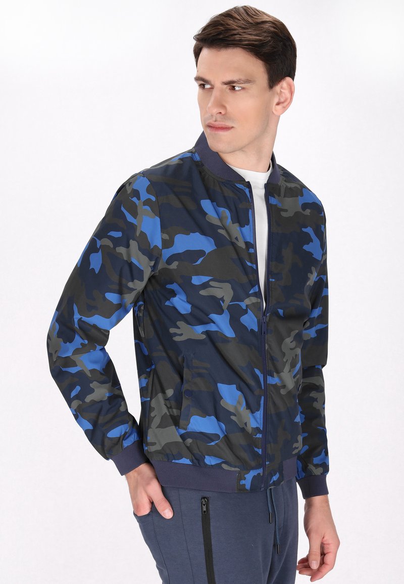 Giacca bomber da uomo con un motivo camouflage in tonalità di blu, grigio e nero, dotata di zip frontale e polsini a costine.