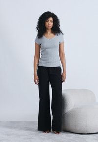 Γκρι εφαρμοστό τοπ με κοντά μανίκια συνδυασμένο με μαύρο παντελόνι πλατύ στο πόδι, με λεία υφή και απλό σχέδιο. Στο βάθος διακρίνεται ένας ανοιχτόχρωμος καμπυλωτός καναπές.