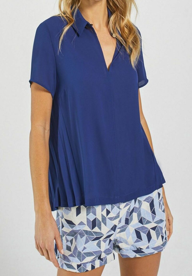 Femme portant un chemisier bleu marine à manches courtes avec un col et un short à motifs géométriques dans des tons de bleu et blanc.