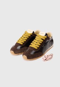 Brązowe zamszowe sneakersy z błyszczącymi czarnymi skórzanymi akcentami i żółtymi sznurówkami. Zawierają dodatkową różową paskowaną sznurówkę. Minimalistyczny design.