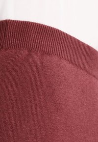 Tessuto a maglia bordeaux con vita a costine, che mostra una texture liscia e un design senza cuciture. Focus sui dettagli di colore e materiale.