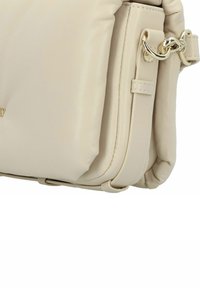 Beige Lederhandtasche mit weichem, gequiltetem Textur, in runder Form und goldenen Hardware-Akzenten an der Seite.