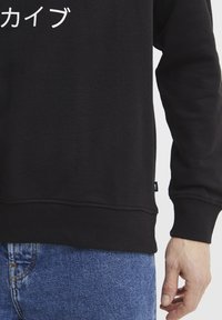 Felpa nera con testo bianco in giapponese, con polsini e orlo a coste, abbinata a jeans in denim blu con un tessuto testurizzato.