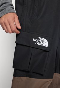 Mustat cargo-shorts, jotka on valmistettu teksturoidusta kankaasta. Ne sisältävät käännettävän taskun, jossa on "The North Face" -logo ja kontrastivärinen ruskea alaosa.