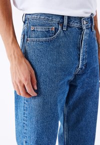 Blå denimjeans i mellem-høj talje med diskret falmning, fem lommer og detaljer i kobber. Struktureret stof.