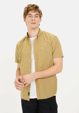 Korte mouwen, knoopshirt in een geel en bruin ruitpatroon, met een borstzak en een wit T-shirt eronder, gedragen met donkere broek.