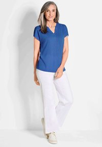 Blauwe top met korte mouwen en een v-hals, gecombineerd met witte flared trousers en beige sneakers. Leverancier met een zachte stof en een relaxte pasvorm.