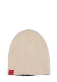 Berretto in maglia beige con una trama liscia, forma arrotondata, dotato di un piccolo etichetta rossa con la scritta "HUGO" di lato.