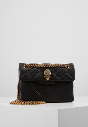 Bolso de mano negro de cuero acolchado con correa de cadena dorada y cierre ornamental de metal dorado con forma de mano, descansando sobre una superficie blanca.