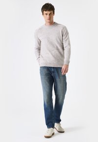 Pull en maille gris clair avec un motif texturé, col rond et bords côtelés. Associé à un jean bleu droit et des baskets blanches.