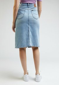 Džínová midi sukně v světle modré, s úzkým pasem, zadními kapsami a rovný střih s třepaným lemem. Kombinováno s bílými teniskami.