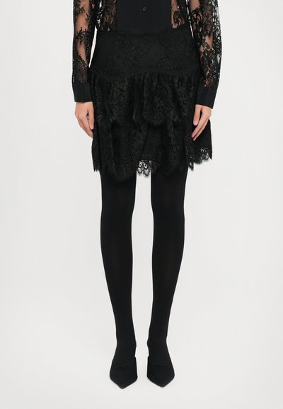 Black lace skirt with layered ruffles and scalloped edges, paired with black opaque tights and pointed-toe heels. Elegant texture and design.