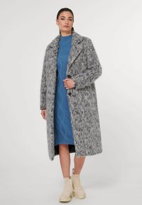 Grau strukturierten langen Mantel mit großem Kragen und Knopfverschluss. Getragen über einem blauen Kabelstrickkleid, kombiniert mit beigen Knöchelstiefeln.