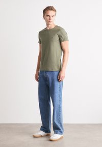 Olivgrünes T-Shirt mit Rundhalsausschnitt und kurzen Ärmeln, kombiniert mit hellblauen geraden Jeans und weißen Sneakers mit beigen Sohlen.
