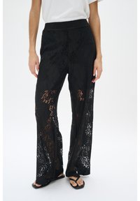 Zwarte lace broek heeft een wijduitlopende pasvorm, gestructureerde stof en bloemmotieven, met een rekbare tailleband en doorschijnende details.