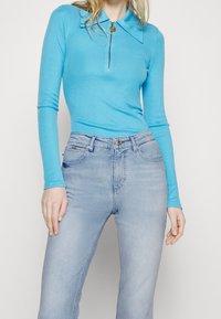 Top de manga larga azul claro con cuello y media cremallera, combinado con jeans de mezclilla claros de corte ajustado y con bolsillos.