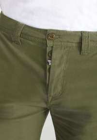 Pantalons kaki avec une texture lisse, dotés d'une fermeture éclair, de deux boutons à la taille et d'un détail de poche cousu.