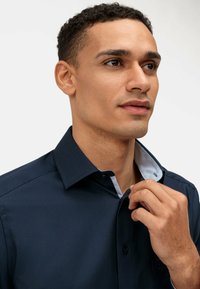 Dunkelblaues Hemd mit Knöpfen und einem kontrastierenden hellblauen Innenkragen, aus glattem Stoff gefertigt, mit einer einzigen Tasche und Knopfdetails.