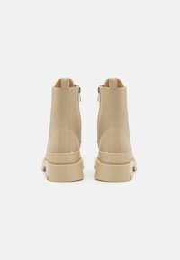 Botas de tobillo beige con un acabado de cuero suave, detalle de cremallera en la parte trasera y una suela de goma gruesa. Punta redondeada y costuras reforzadas visibles.