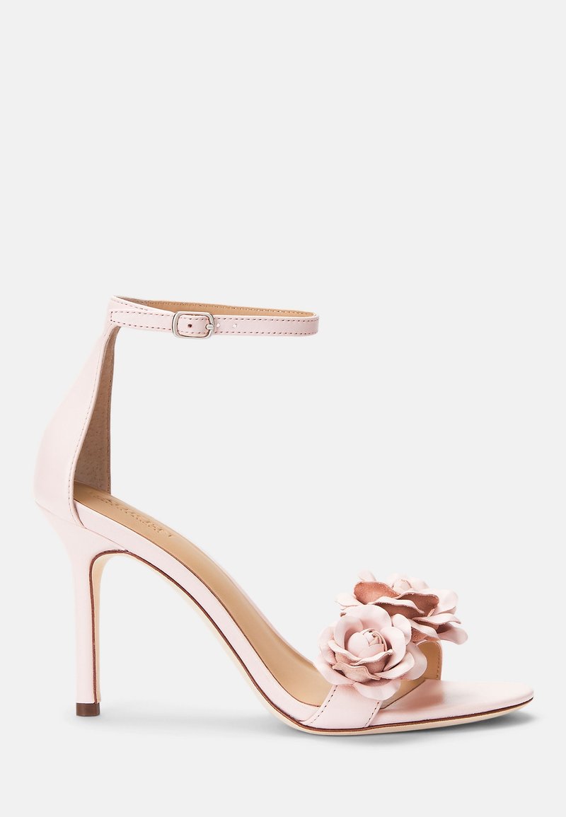 Różowe sandały na wysokim obcasie z paskiem wokół kostki, z dwoma dekoracyjnymi różami z tkaniny z przodu oraz gładką skórzaną teksturą.