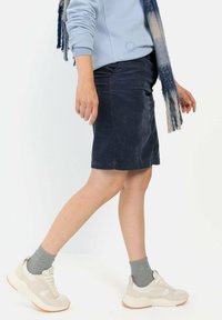 Knielange marineblaue Cordrock, kombiniert mit hellgrauen Socken und weißen Turnschuhen, mit einer strukturierten Oberfläche und subtilen Details.