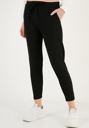 Black jogger pants made of a soft fabric, featuring a drawstring waist, side pockets, and tapered ankles, paired with white sneakers.