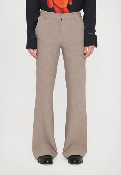 Pantaloni beige a vita alta realizzati in tessuto testurizzato, con un design a gamba svasata. Abbinati a una blusa scura con motivo e scarpe nere.
