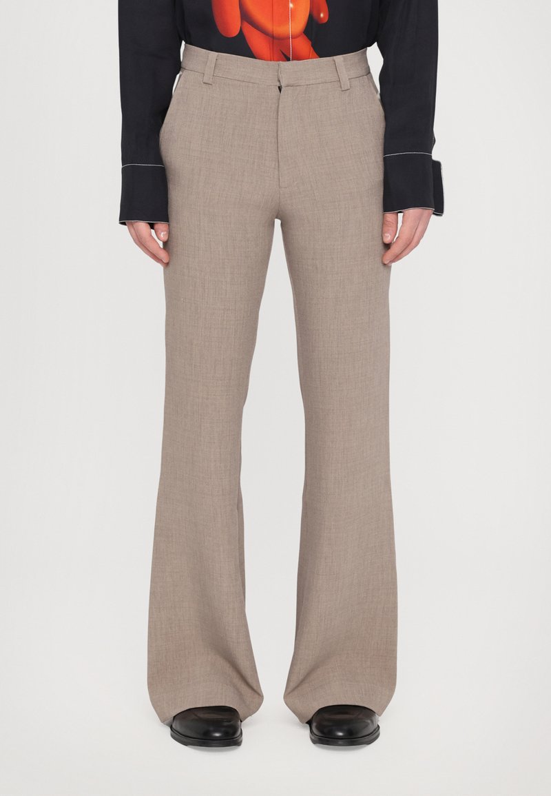 Beige, high-waisted trousers made of textured fabric, featuring a flared leg design. Paired with a dark patterned blouse and black shoes.